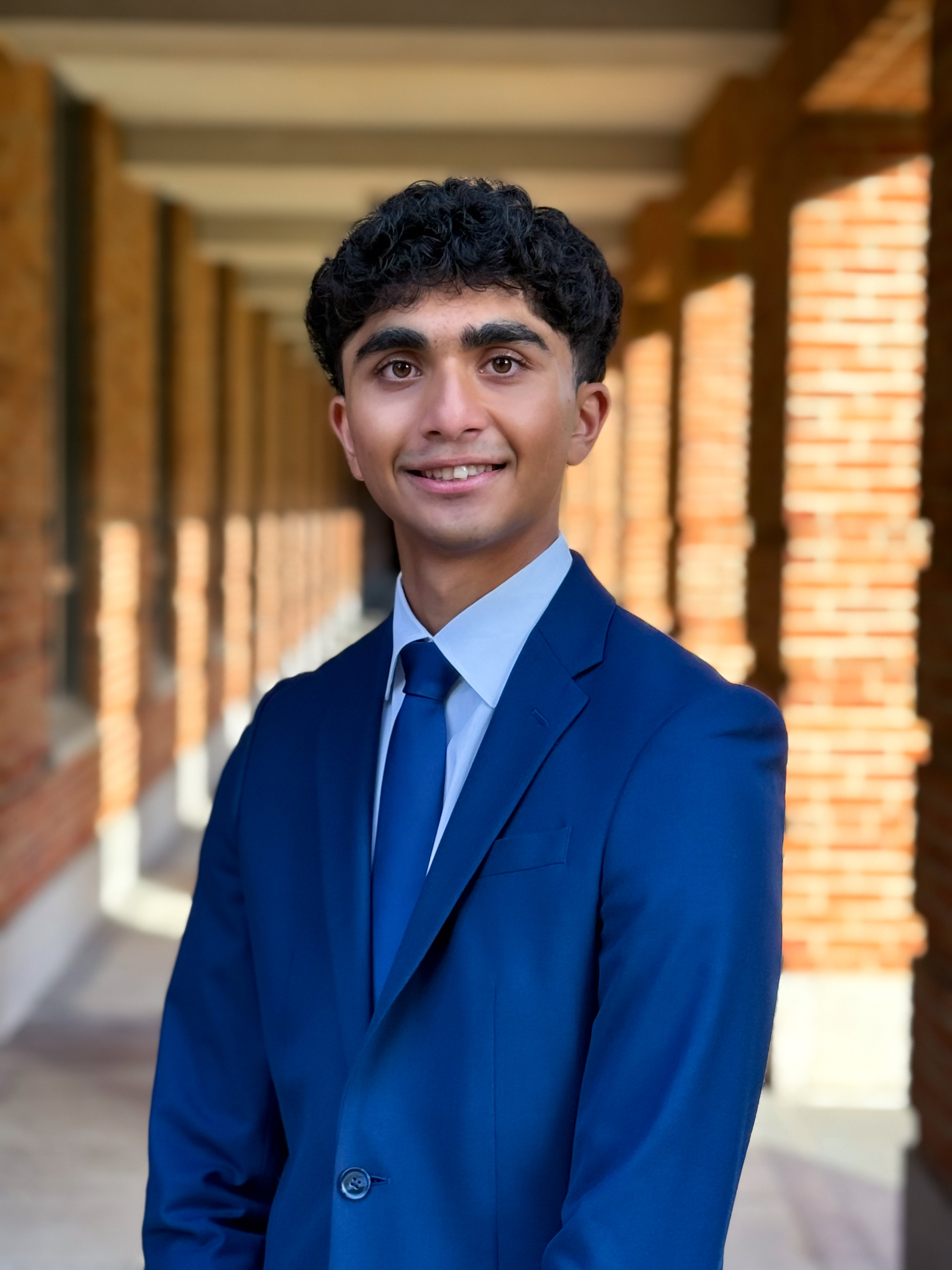 man smiling at camera with navy blue suit, light blue dress shirt, and solid blue tie