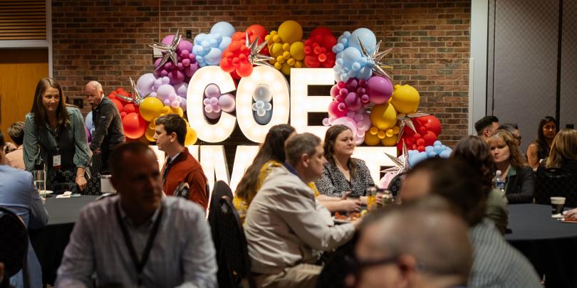 Crowded ballroom with COE marquee letters in background