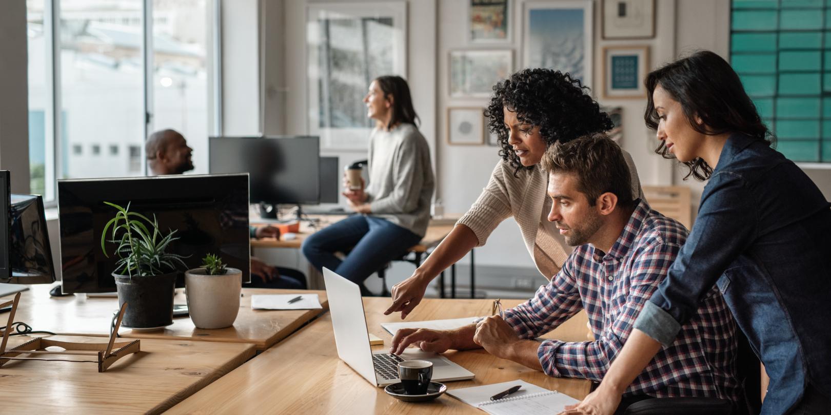 3 people looking at a laptop in an office