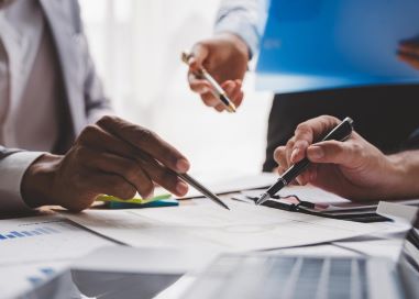 3 people with pens in their hands looking over a document