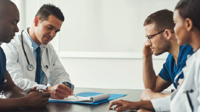4 medical professionals at a table discussing documents