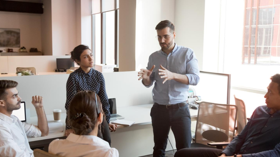 A young leader speaking to 4 other professionals in a meeting