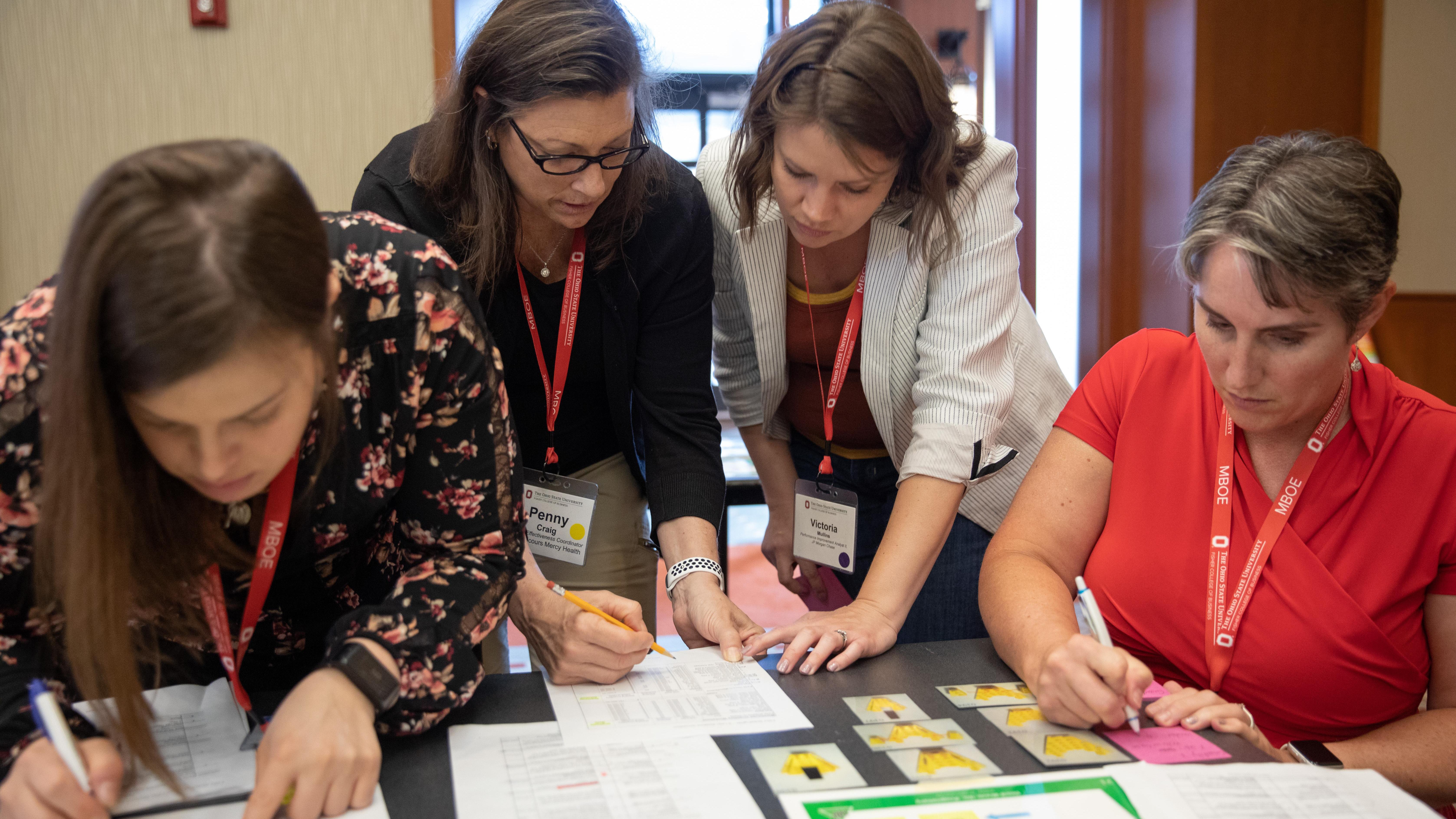 4 women working together at a table with papers