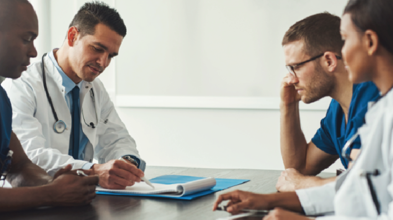 4 medical professionals at a table discussing documents