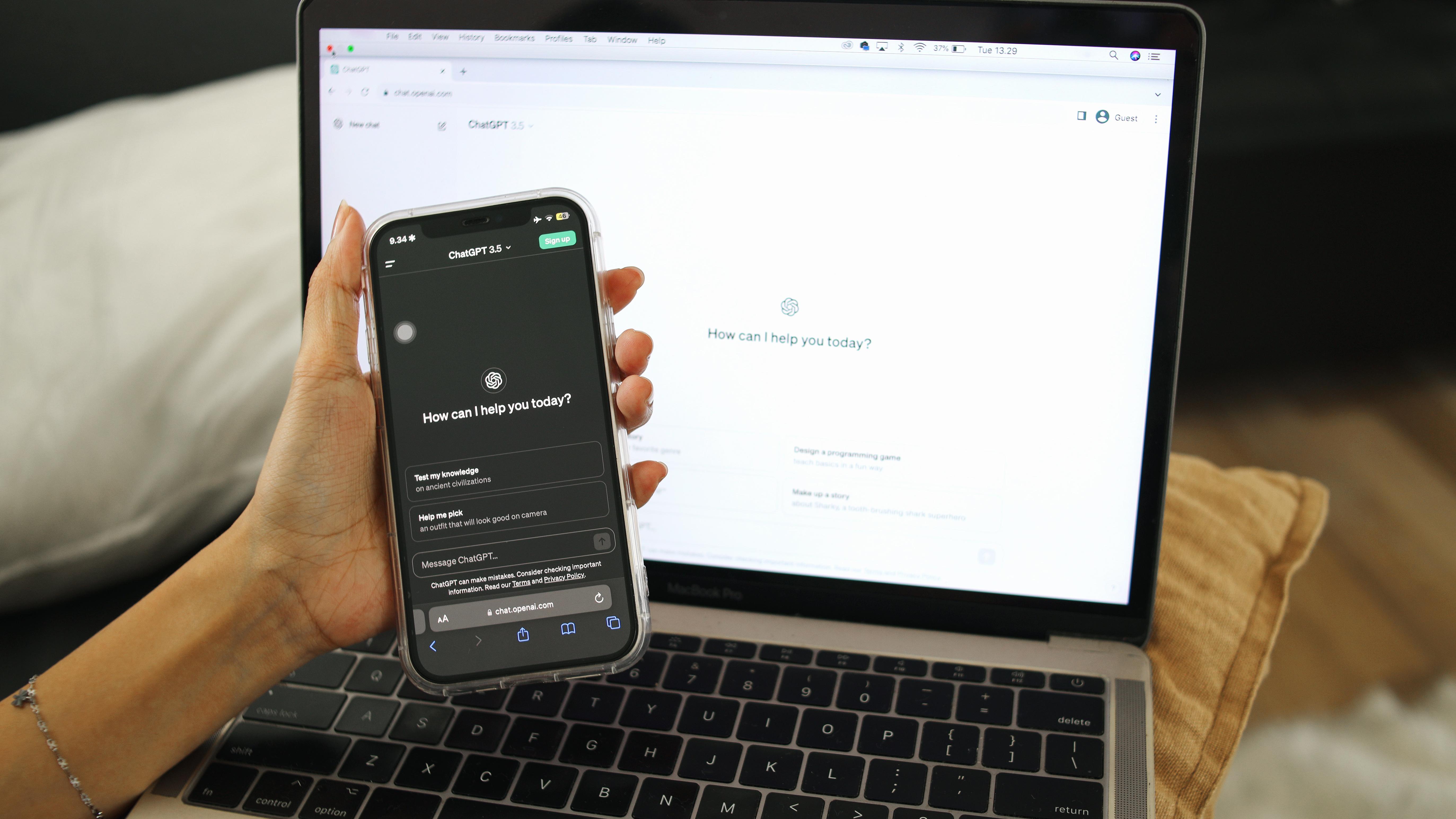 A hand holding a phone with ChatGPT open on it in front of a laptop
