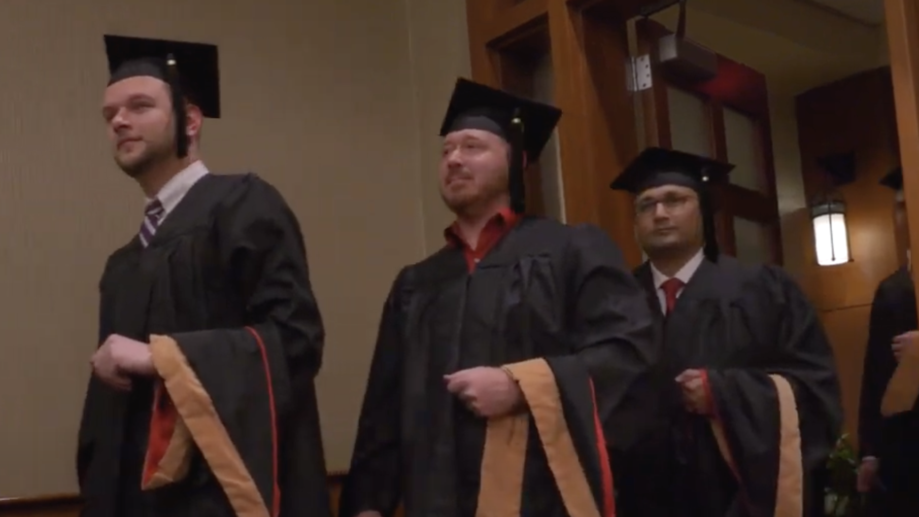 Three students standing in graduation caps and gowns