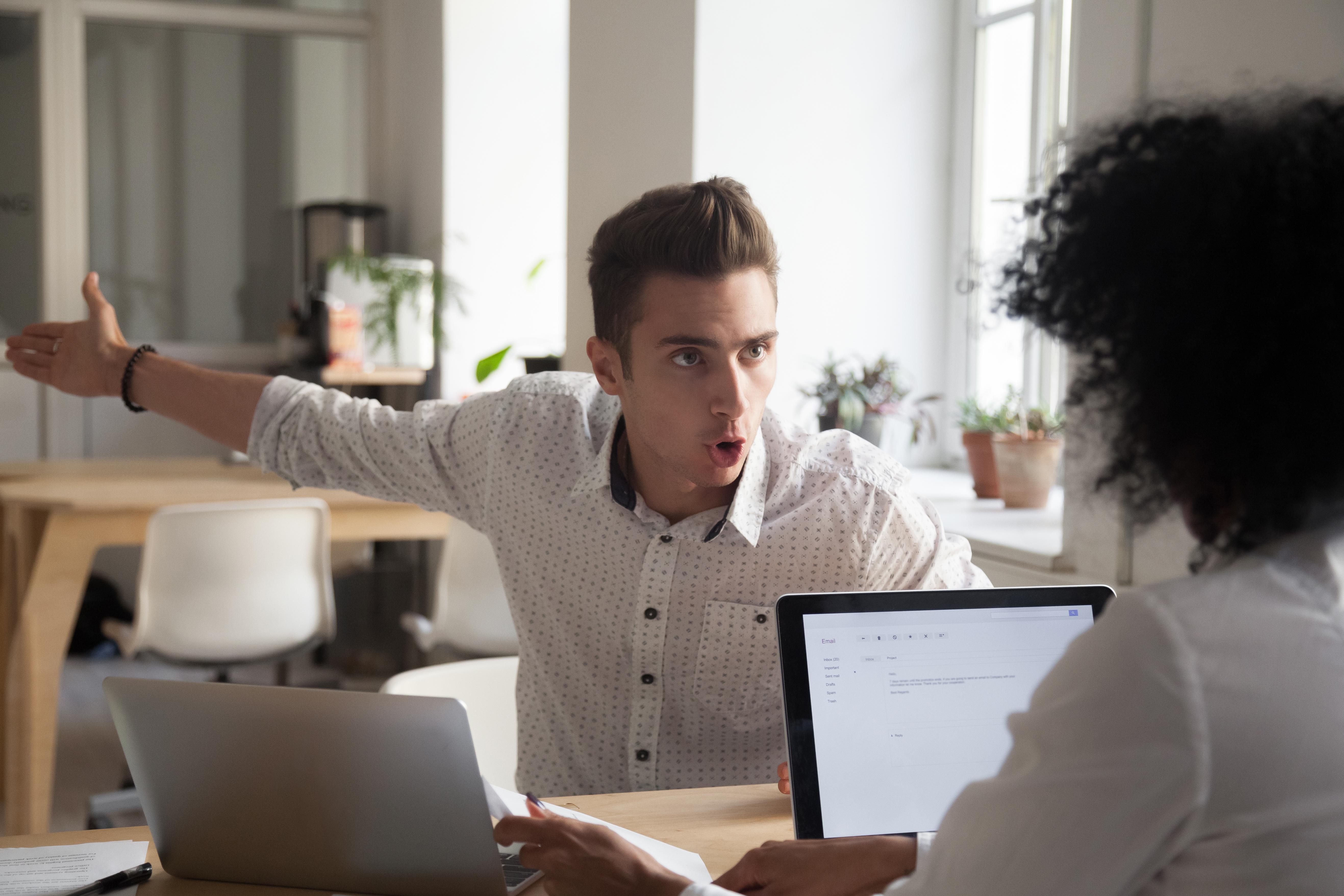 Man in office complaining to a woman seated across from him 