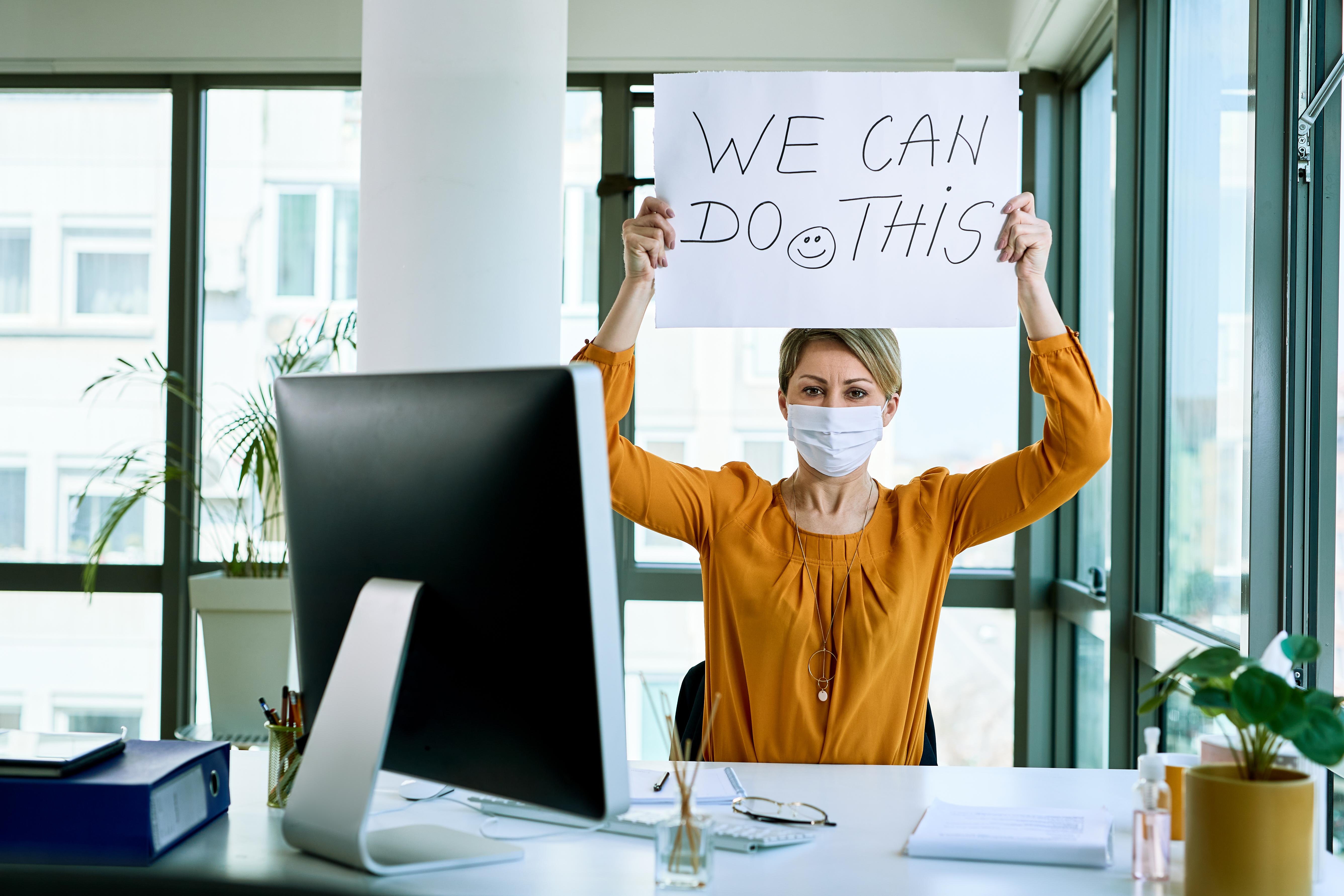 Woman in mask holding up "We Can Do This" sign