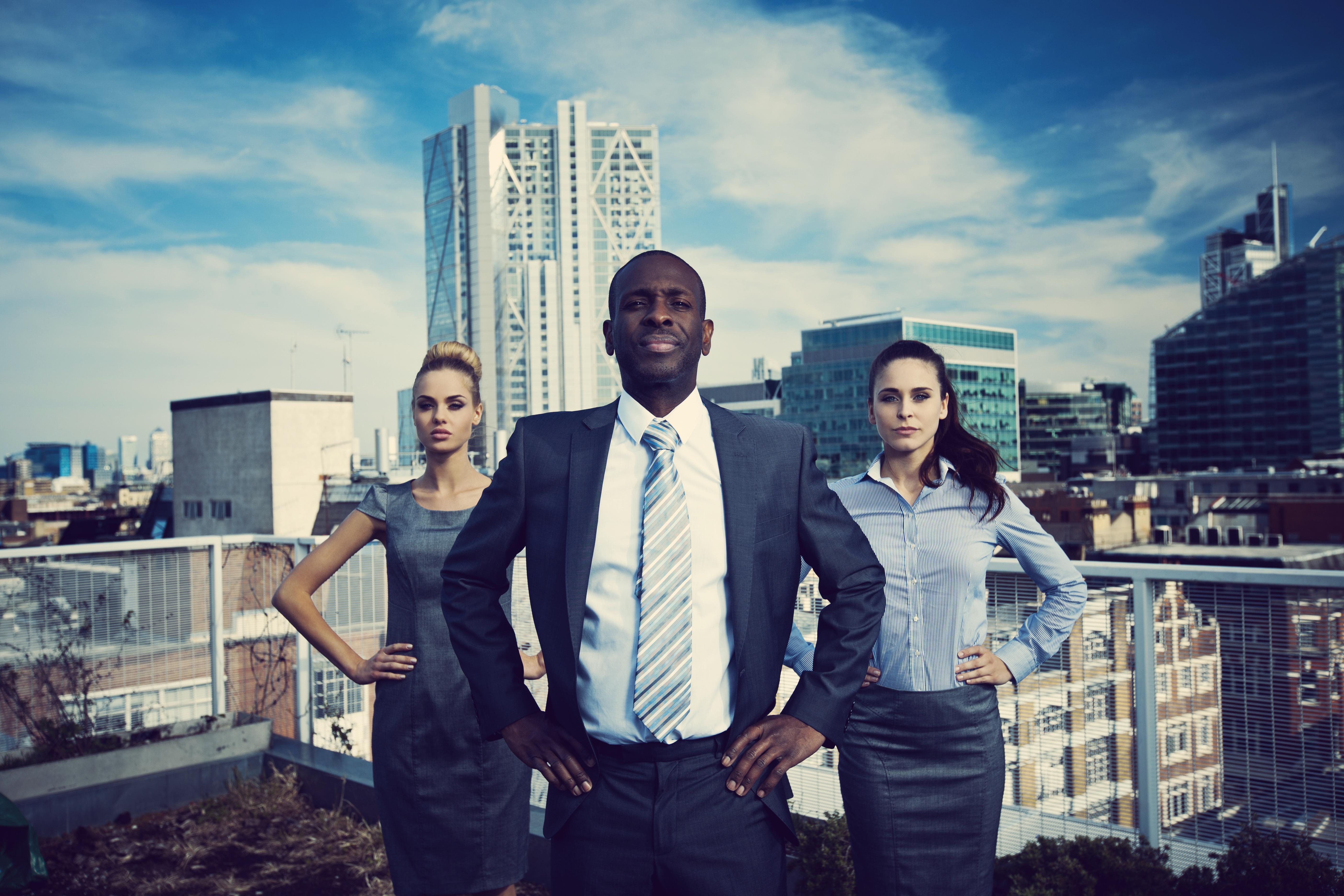 Three businesspeople posing like superheroes on a roof