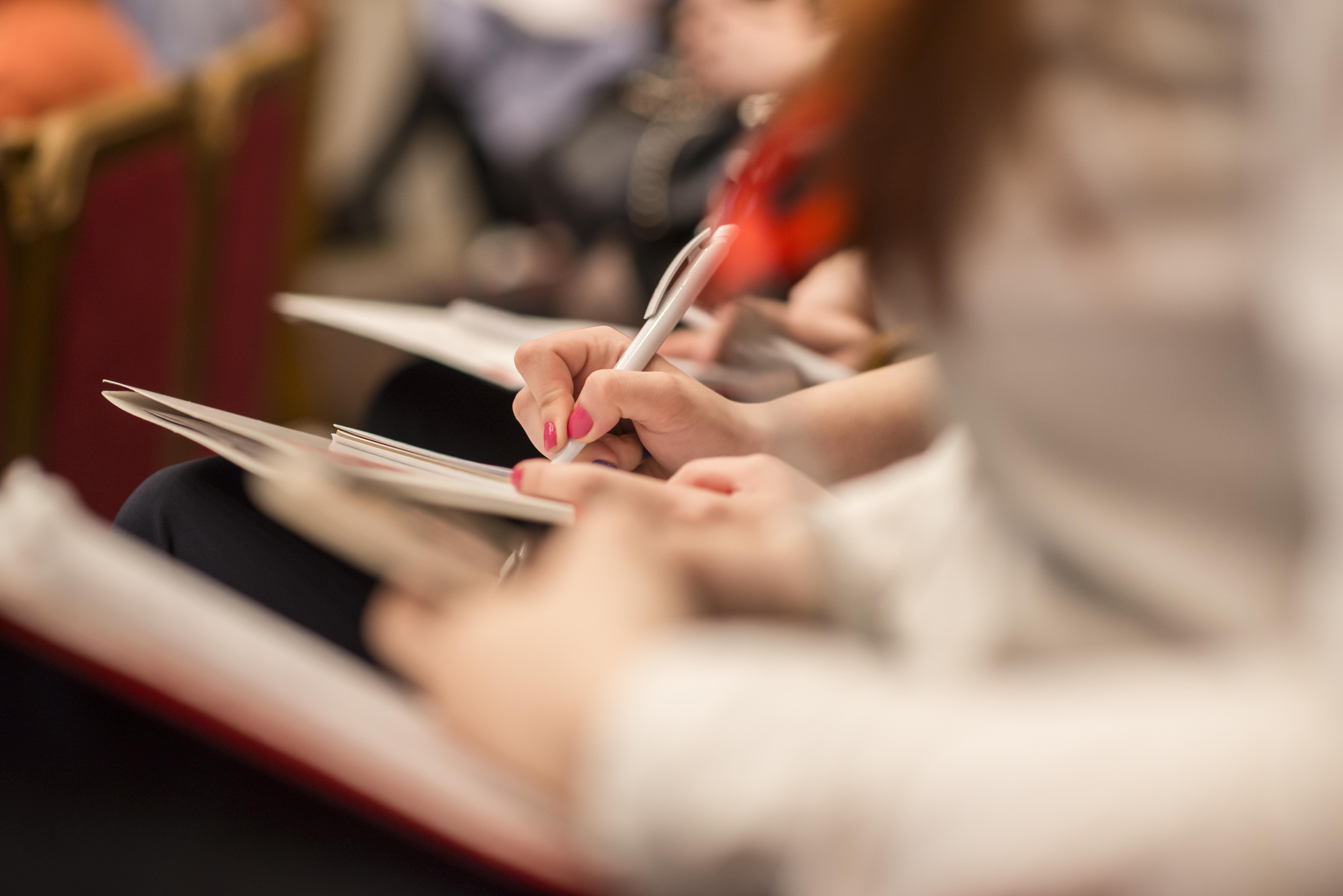 Closeup of people's hands taking notes at a seminar 