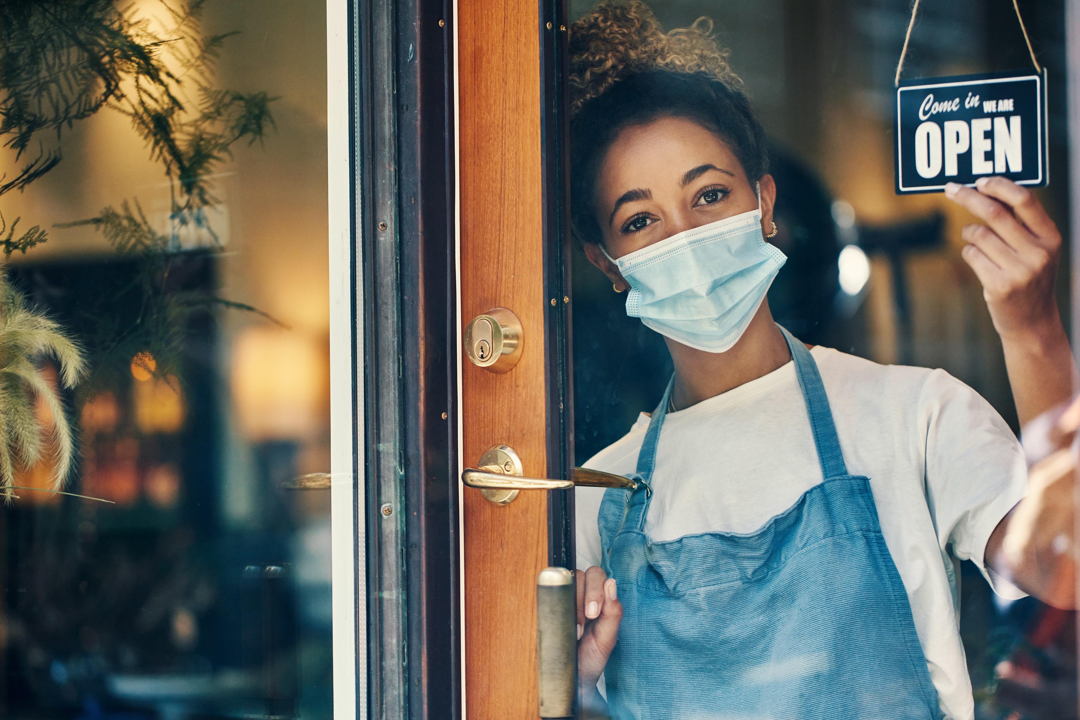 Business owner with mask on flipping door sign to open