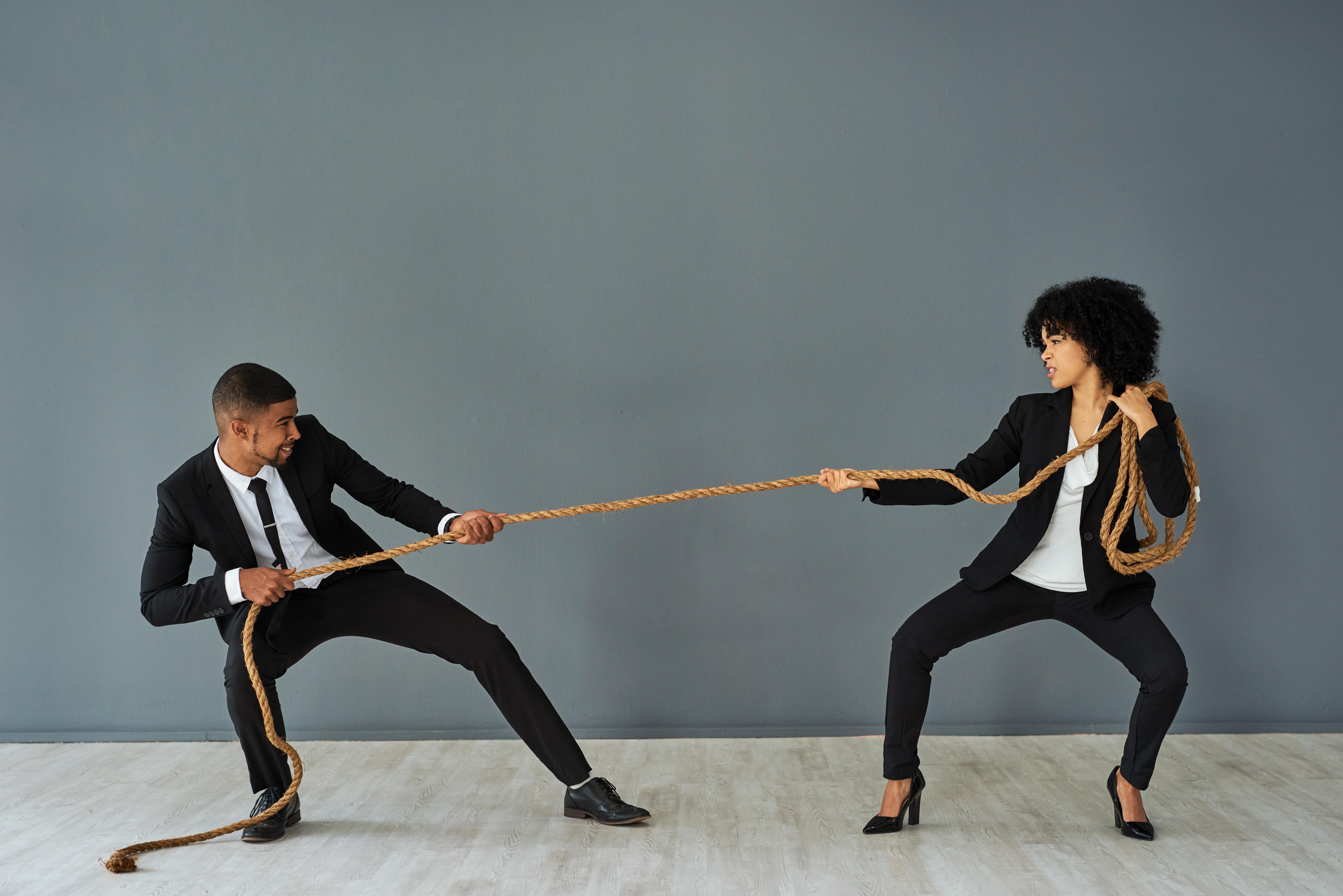 A man and a woman in business clothes playing tug of war 