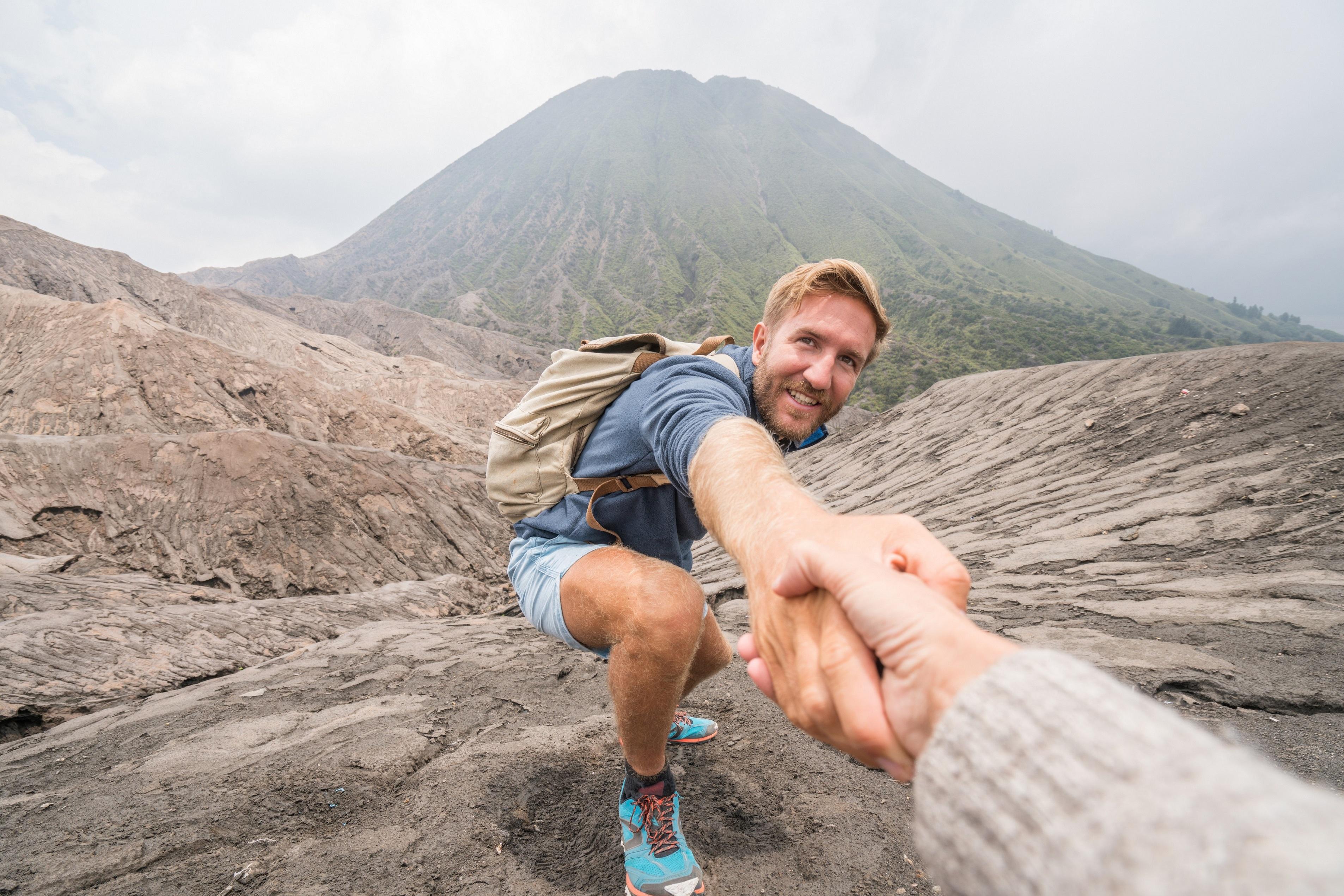 hand reaching out to help pull man up a mountain