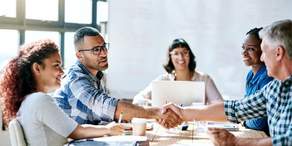Two individuals shake hands across a meeting room table