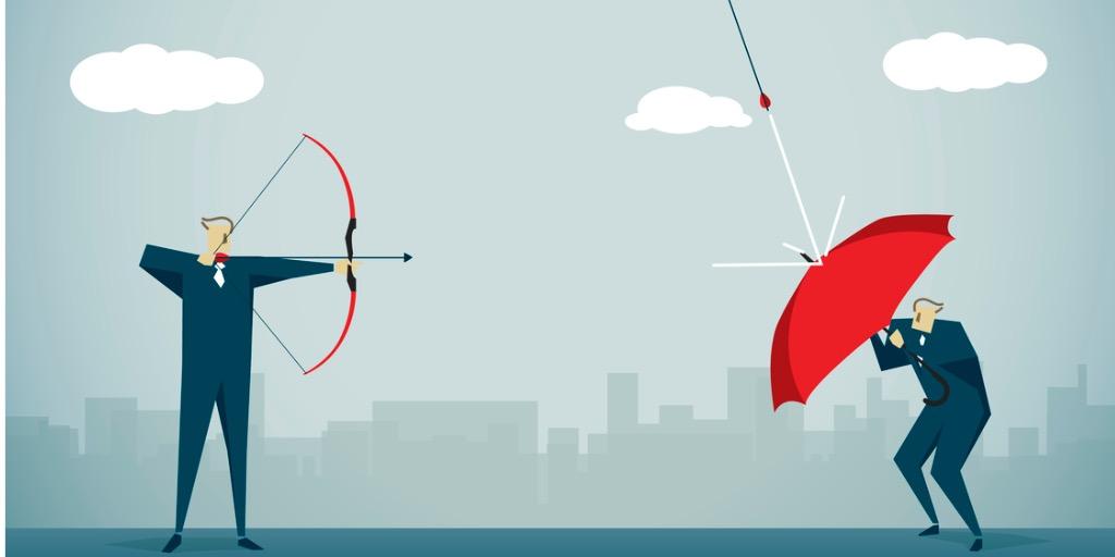 Businessman aiming arrow at businessman trying to protect himself with umbrella 