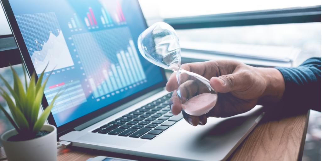Businessman holding hourglass with chart on computer in background