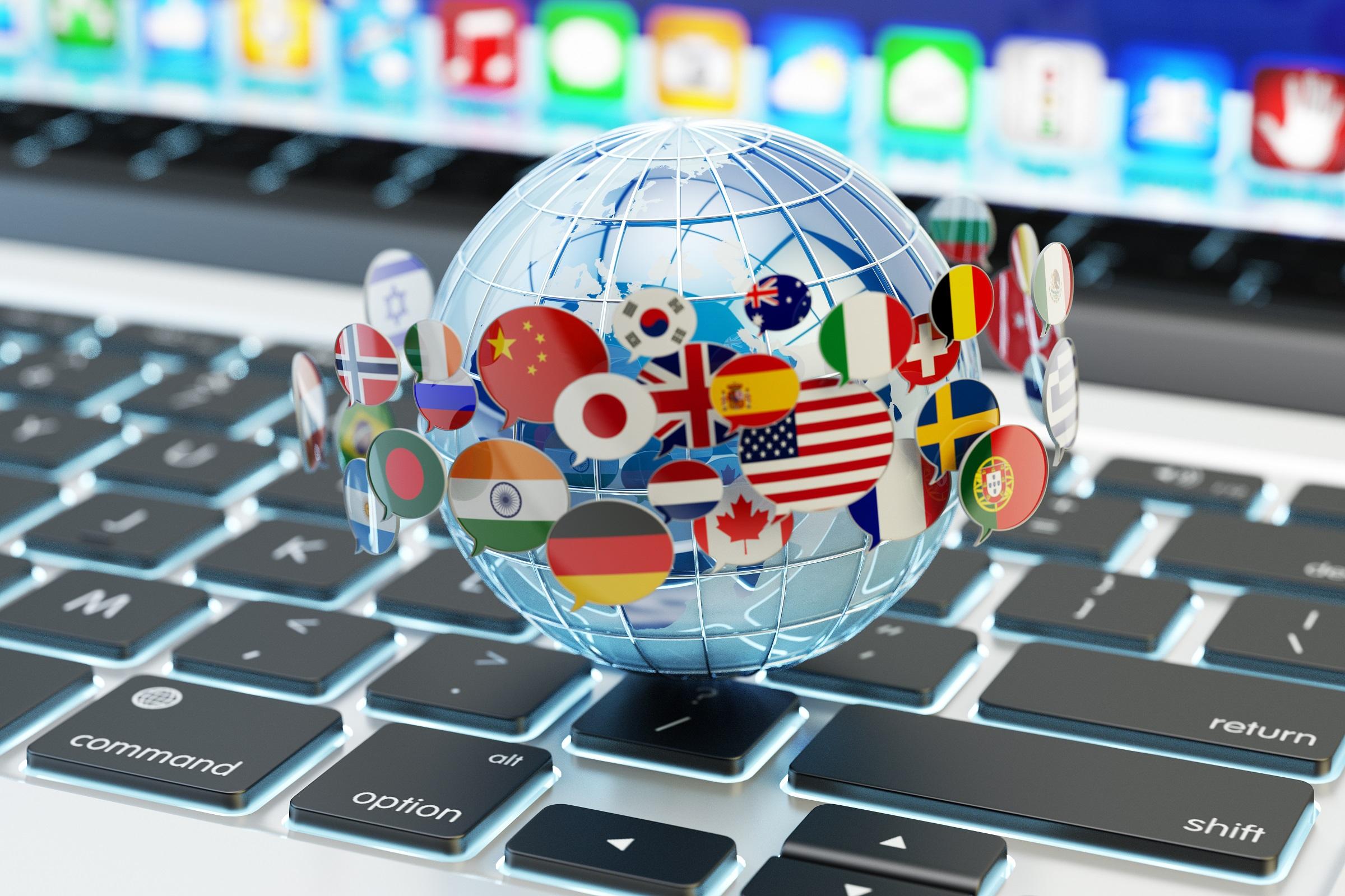 globe covered in speech bubbles with different countries' flags sitting on a laptop keyboard