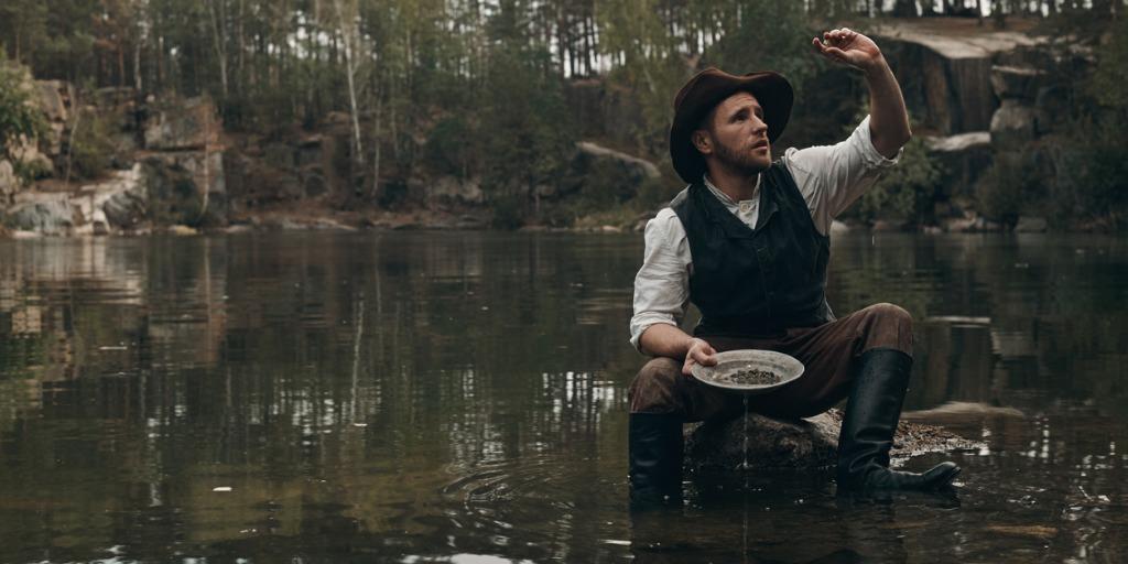 Man in boots and cowboy hat sifting through stones in a creek