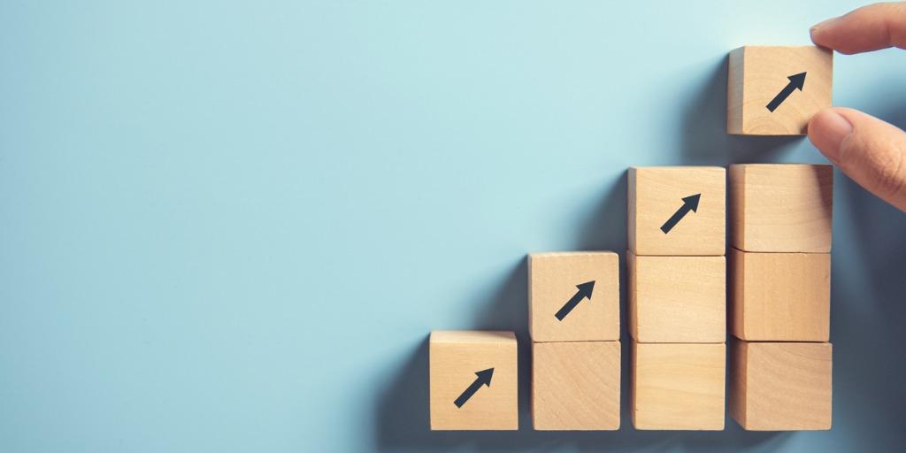 Person piling blocks of columns, each one block higher, with an arrow on the top showing increased progress