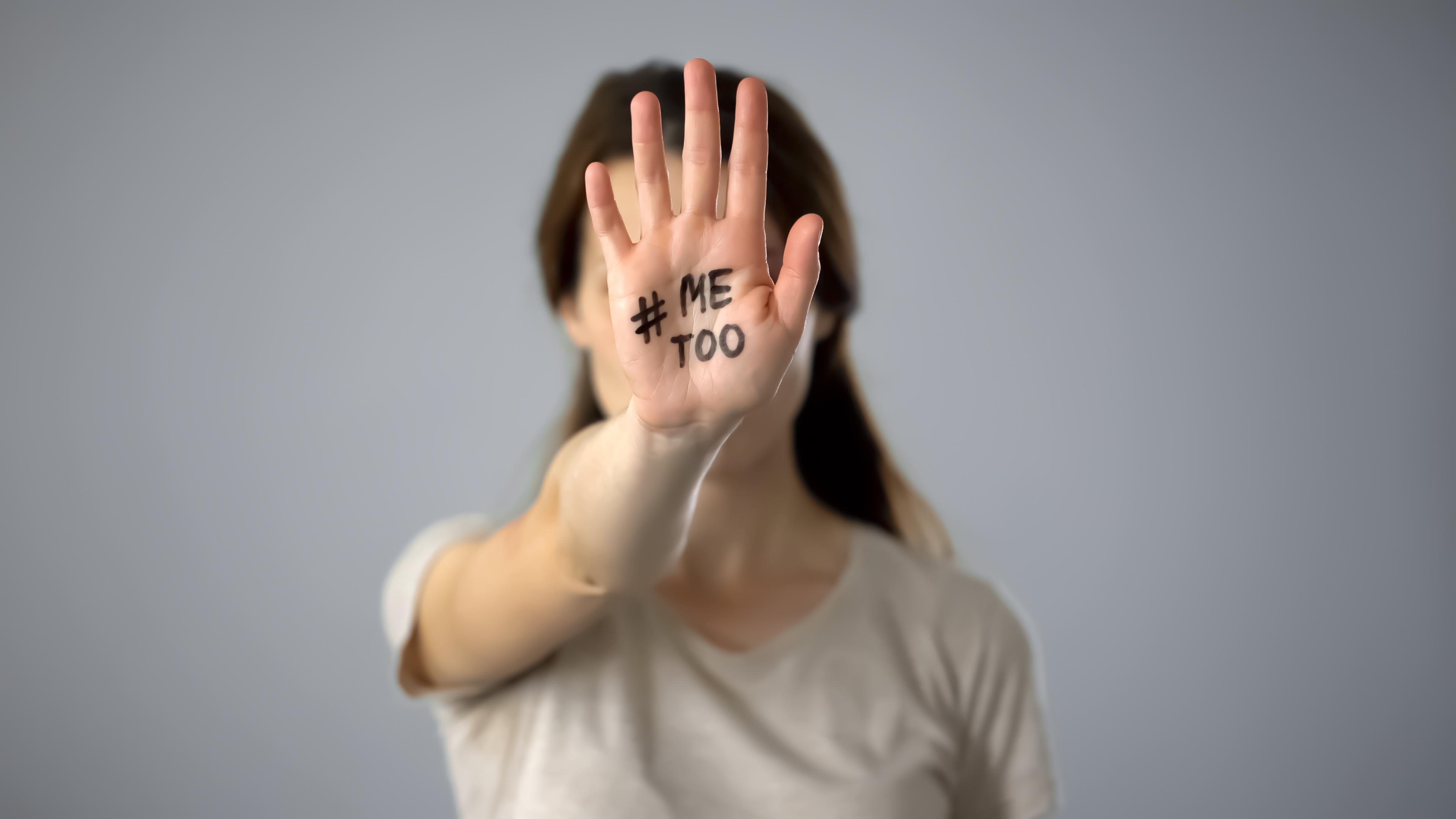 Woman covering her face by holding out hand with "#metoo" written on it