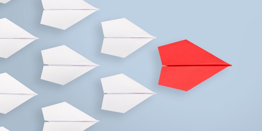 Red paper airplane is leading other white paper airplanes fly