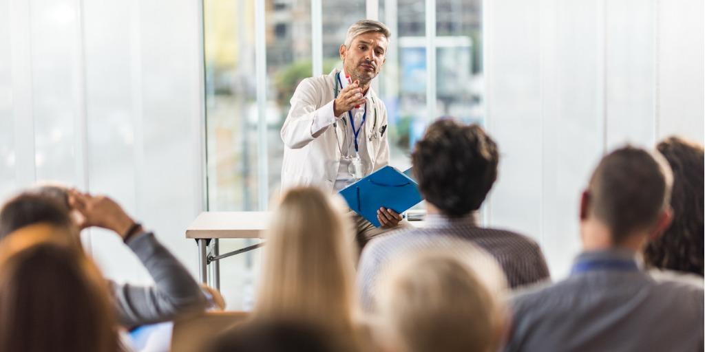 Man in lab coat presenting to group of listeners