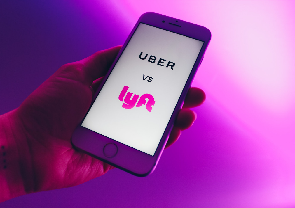 Hand holding cell phone that reads "Uber vs. Lyft" on the screen