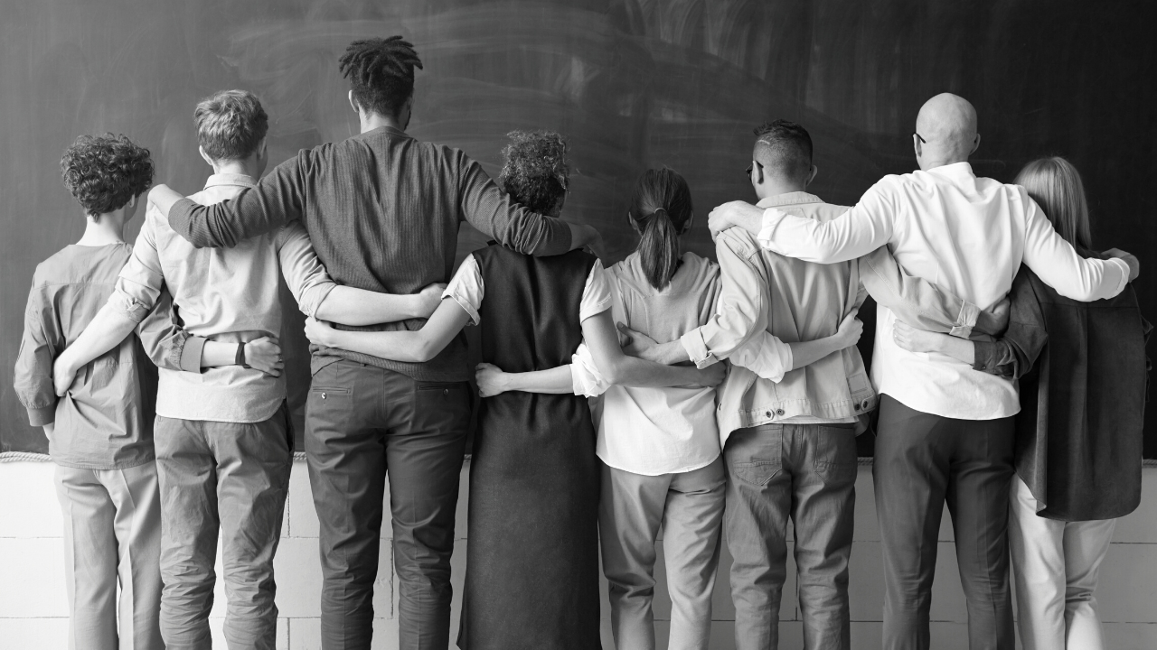 Diverse group stand arm in arm with their backs facing the camera