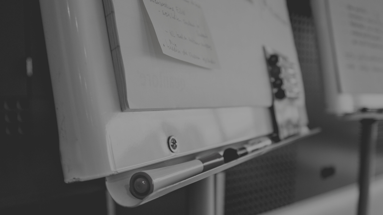 Black and white image of a white board with post it notes on it and markets resting on the bottom.