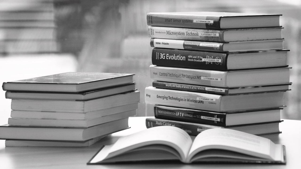 Black and white image of books stacked on a table