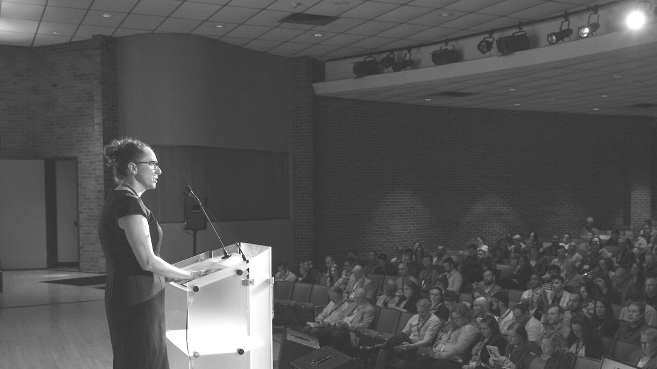 Woman speaking at podium with onlooking audience
