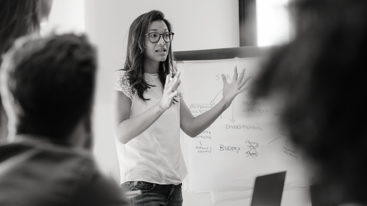 Black and white image of women standing and presenting in front of a whiteboard
