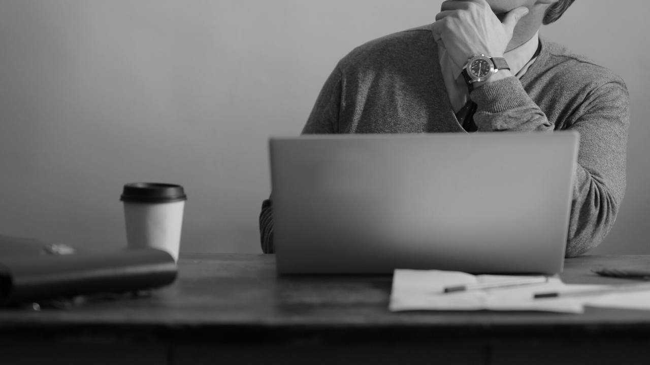 Man at open laptop with hand on chin, implying thinking