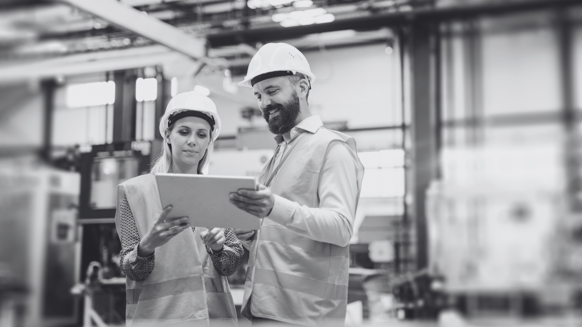 Two people wearing hard hats look at a clipboard
