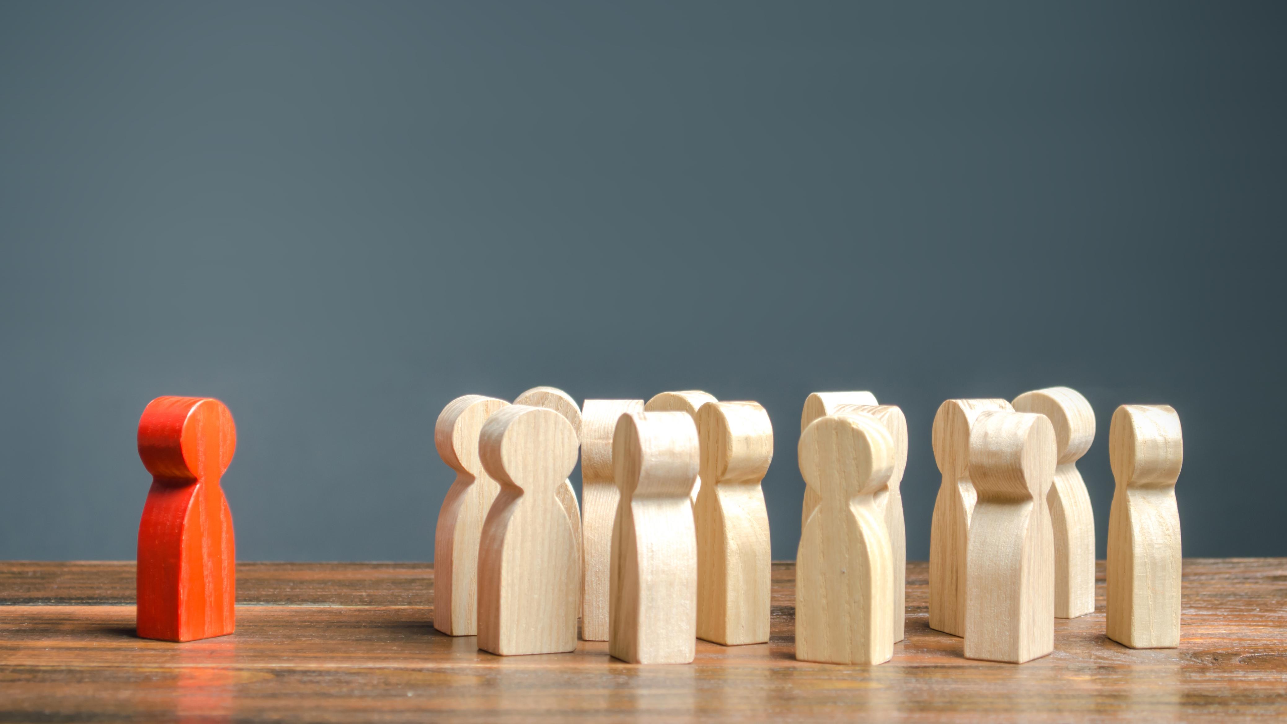Red person block standing out from group of wooden people blocks
