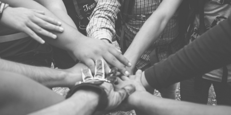 black and white image of hands coming together in a huddle; red text box overlay with white text that reads: Top 5 Ways OpEx Enhances Collaboration 