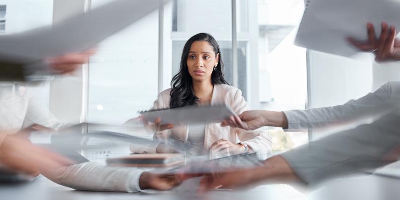 Woman seated looking stressed while papers are passed in front of her