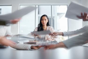 Woman seated looking stressed while papers are passed in front of her