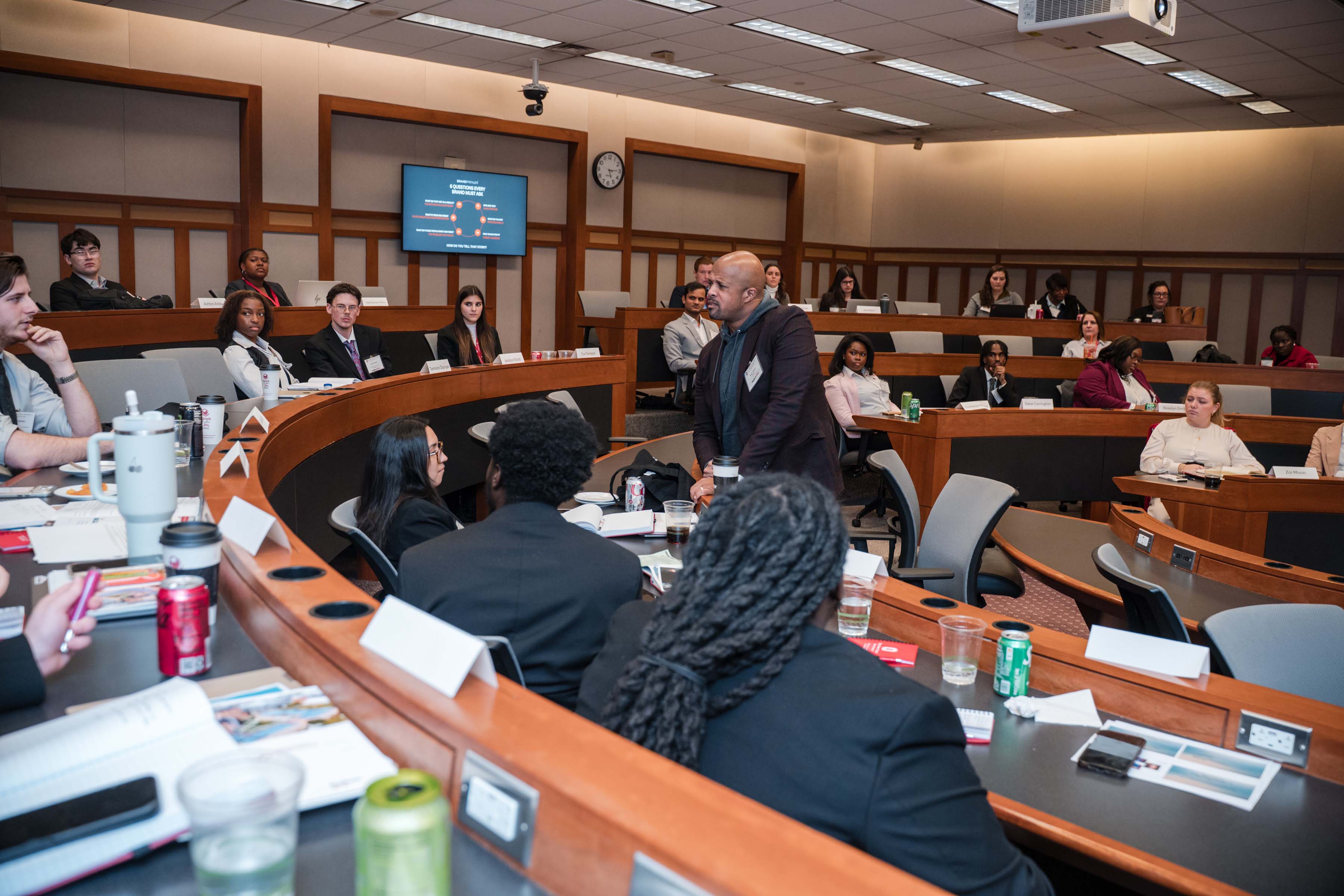 Speaker engaging with student participants in a tiered classroom during an academic symposium.