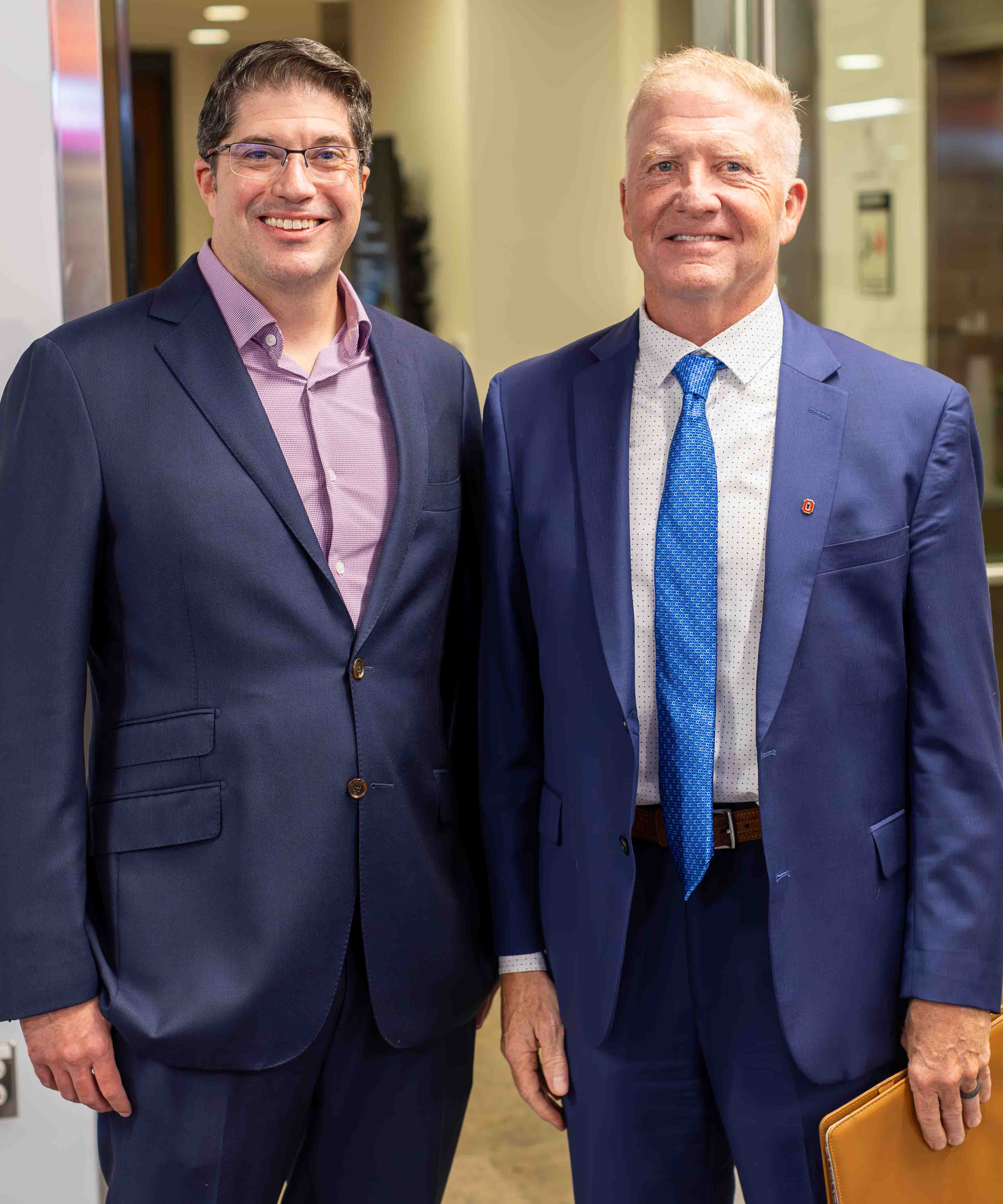 Matt Sheridan, in a blue suit and lavender shirt, stands to the left of Dave Jacobs, wearing a blue suit jacket, blue tie and an Ohio State lapel pin.