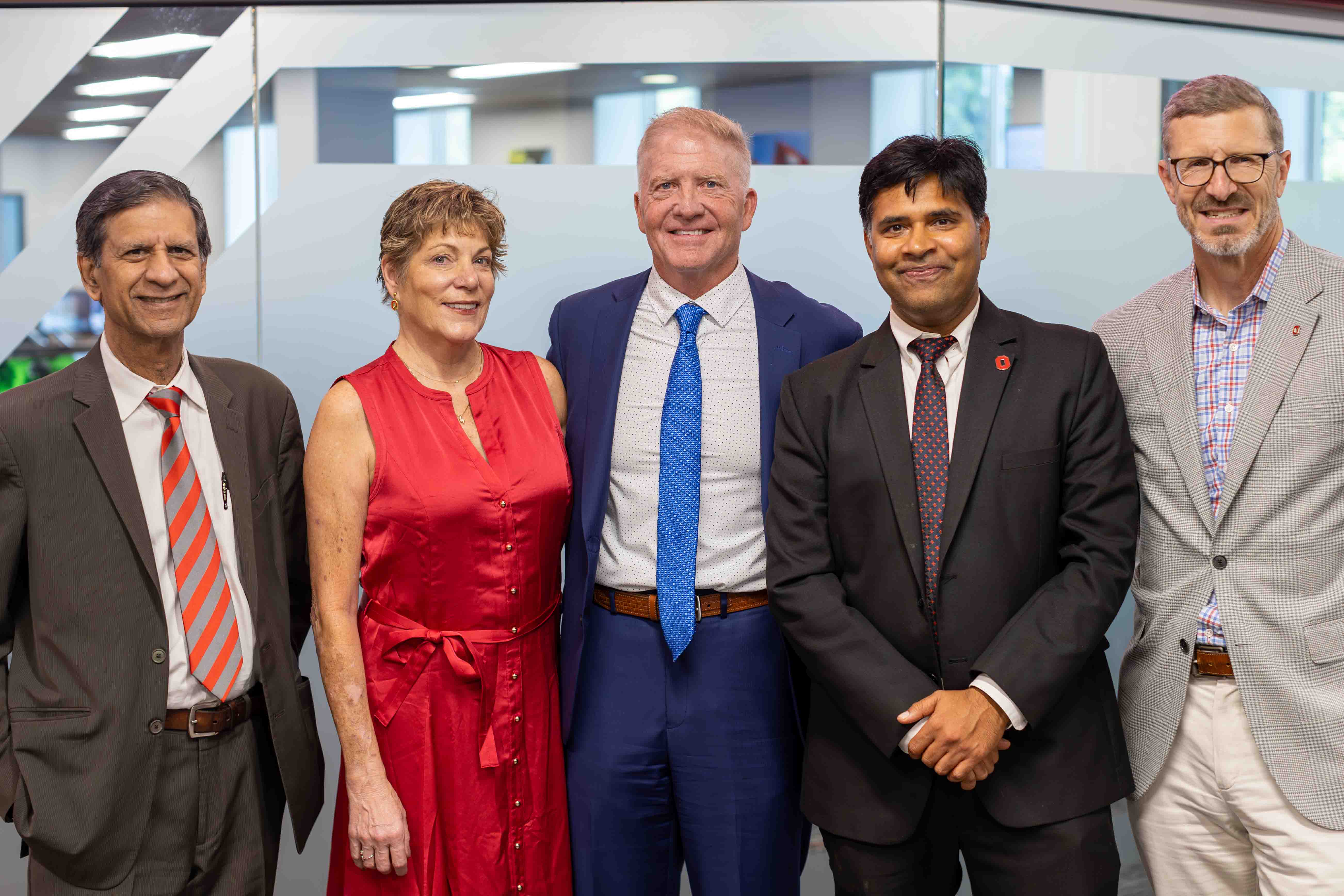 Former Fisher Dean Anil K. Makhija, Brenda Jacobs, Dave Jacobs, current dean Aravind Chandrasekaran, and former interim dean Trevor Brown stand in front of the glass doors of the new business lab.