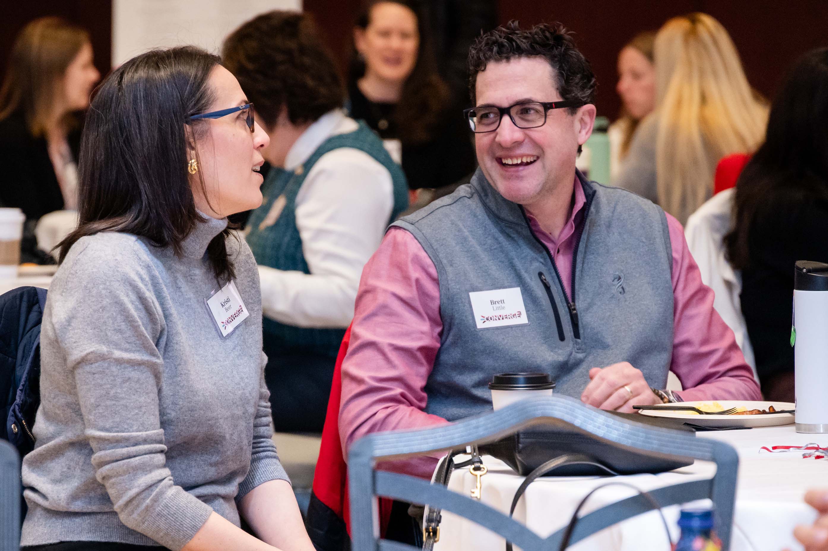 Brian Little is seated at a table talking with another conference attendee.