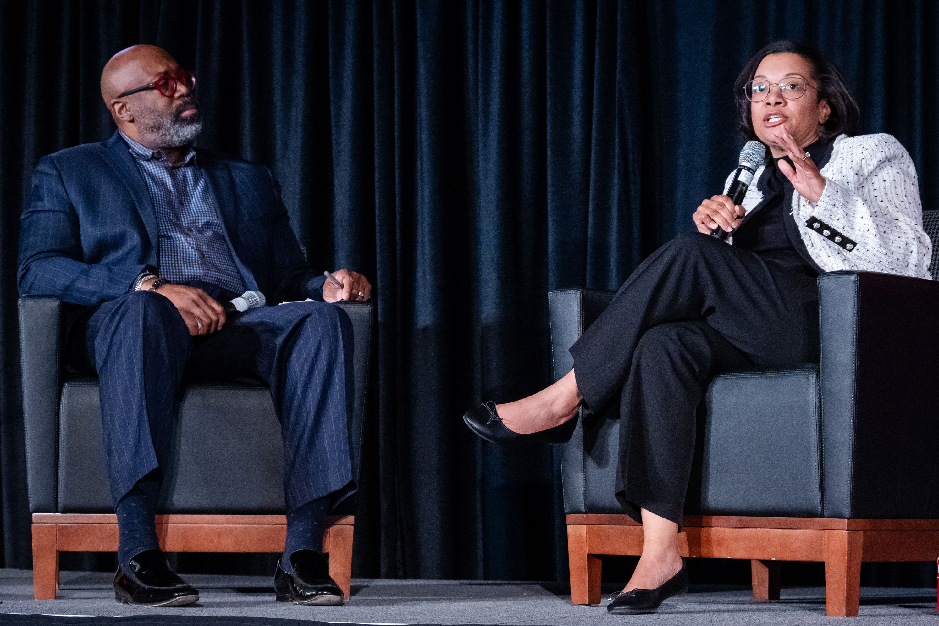 Terry Esper, left, and Jana Croom, right, are seated in gray leaterh chairs on the stage holding microphones.