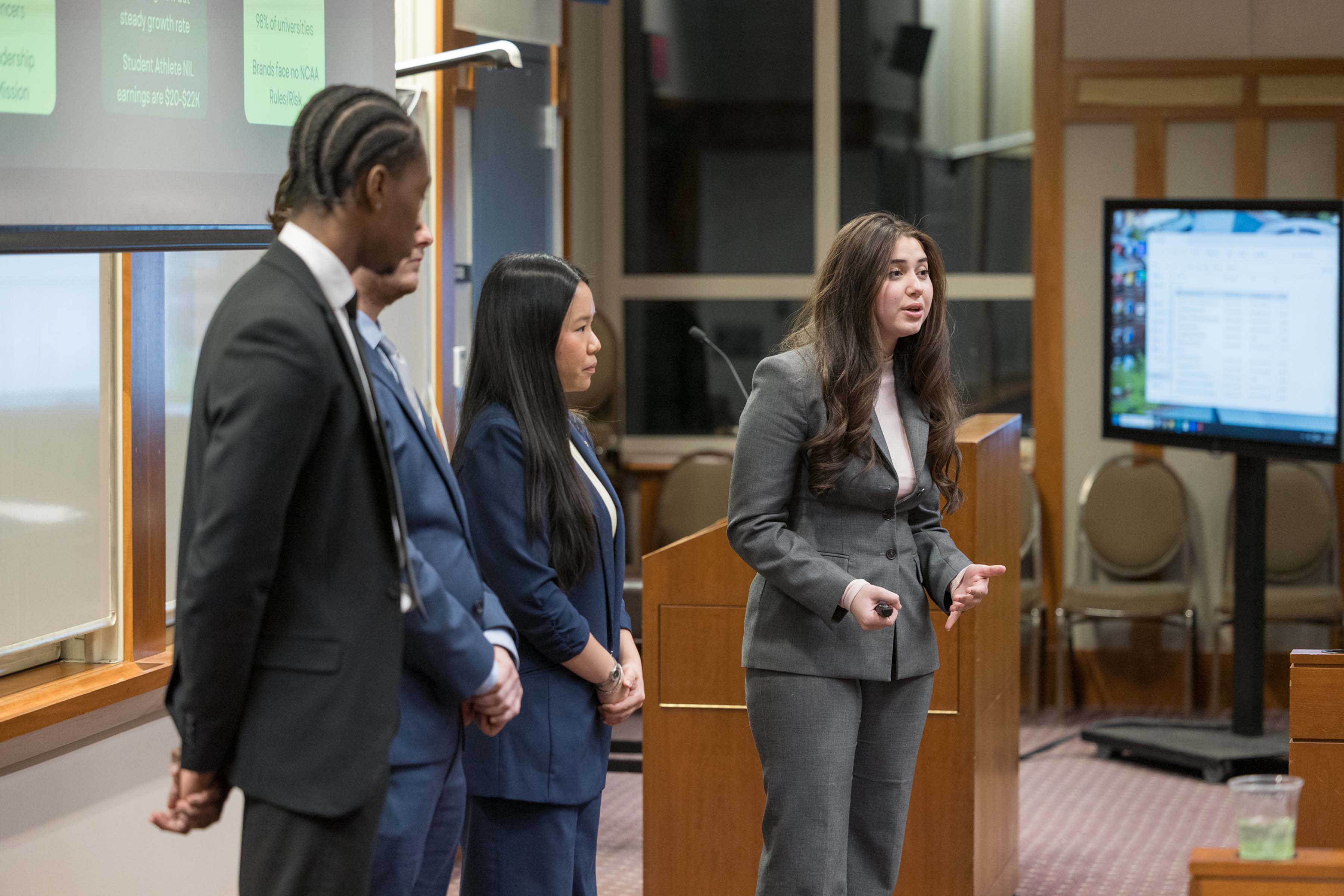 A group of presenters standing at the front of a classroom giving a professional presentation.