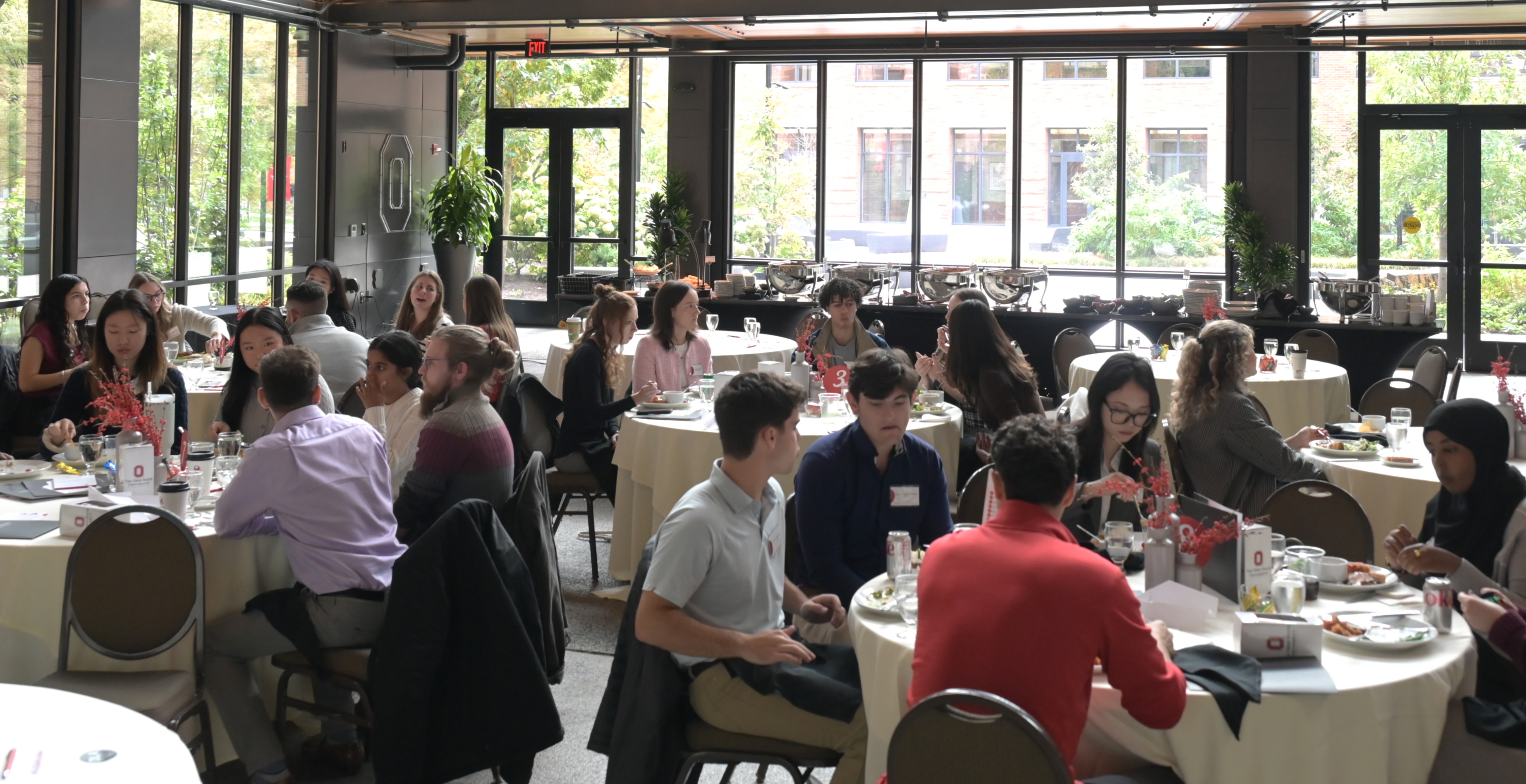 Students, alumni and faculty sitting at round tables eating lunch.