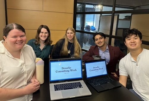 Five students sitting in conference room with two computers displaying Desafio consulting work