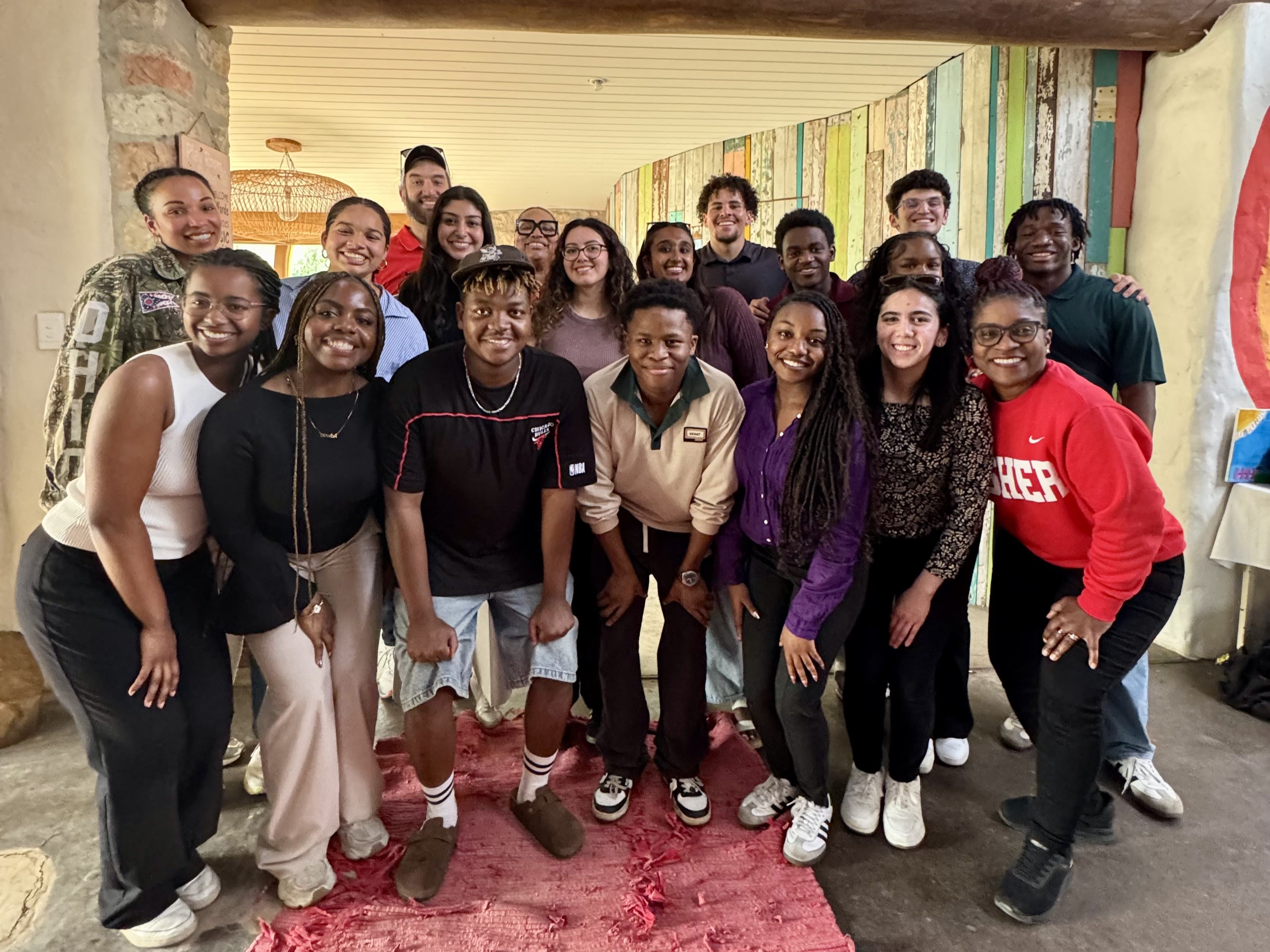 Group of students standing together indoors, posing for a group photo in a colorful hallway.