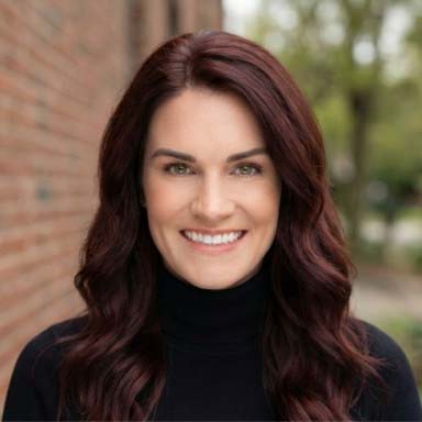 Headshot of Chelsea Dreven in a black turtleneck outside with red brick and green trees blurred in the background.