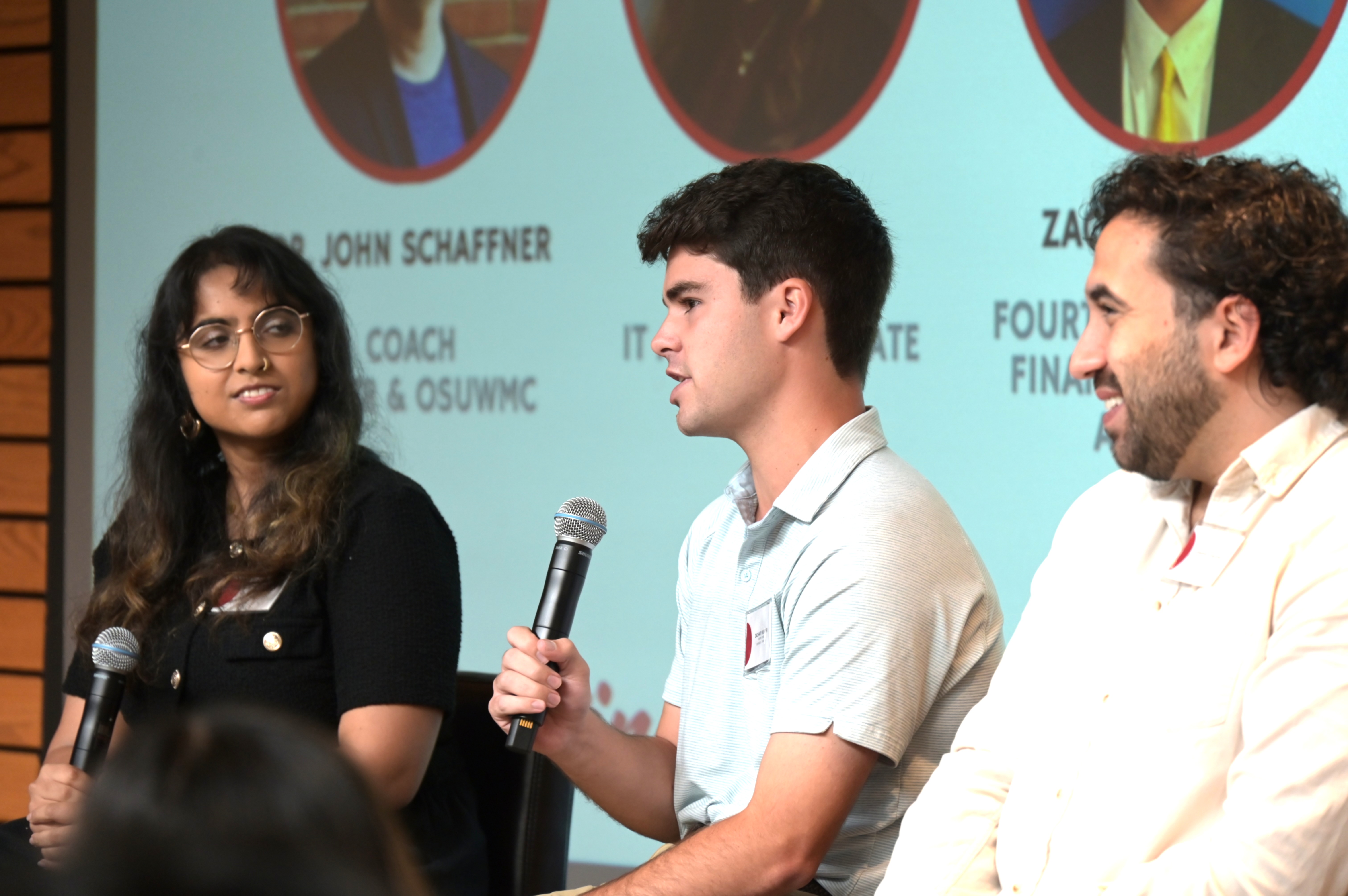 Two students and an alumnus are seated as part of a panel discussion. The students are holding microphones.