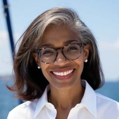 Headshot of Dana Sadiq wearing a white blouse against a blue sky background.